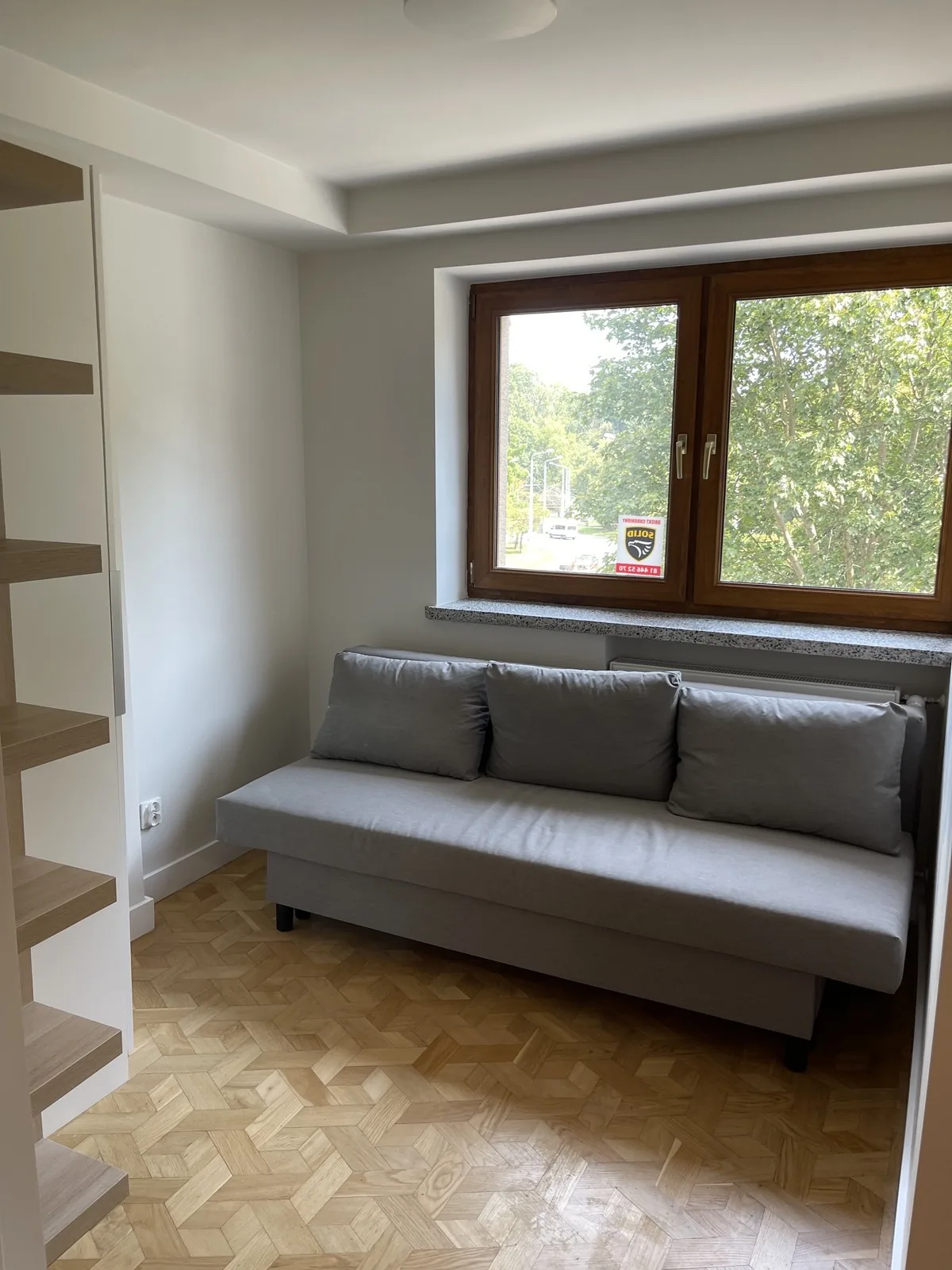 Salon z szarą sofą i oknem na drzewa